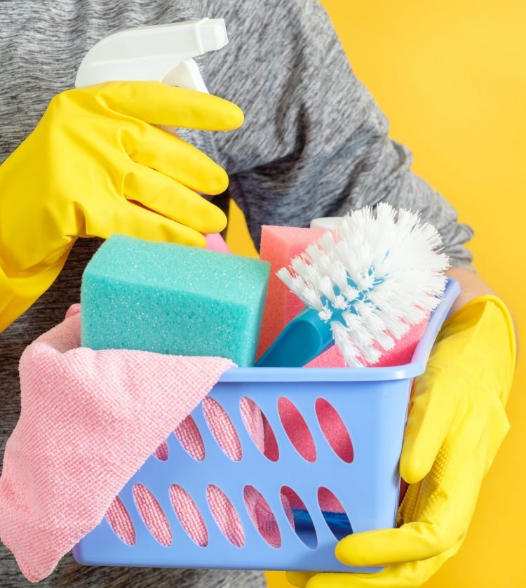 House cleaning. Spring cleanup. Torso with basket of supplies. Copy space on yellow background.